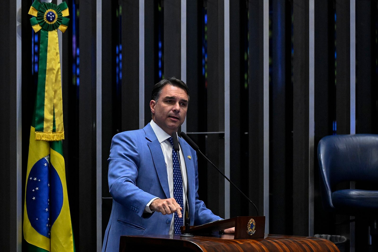 Senador Flávio Bolsonaro discursa na tribuna do plenário do Senado, com a bandeira do Brasil ao fundo