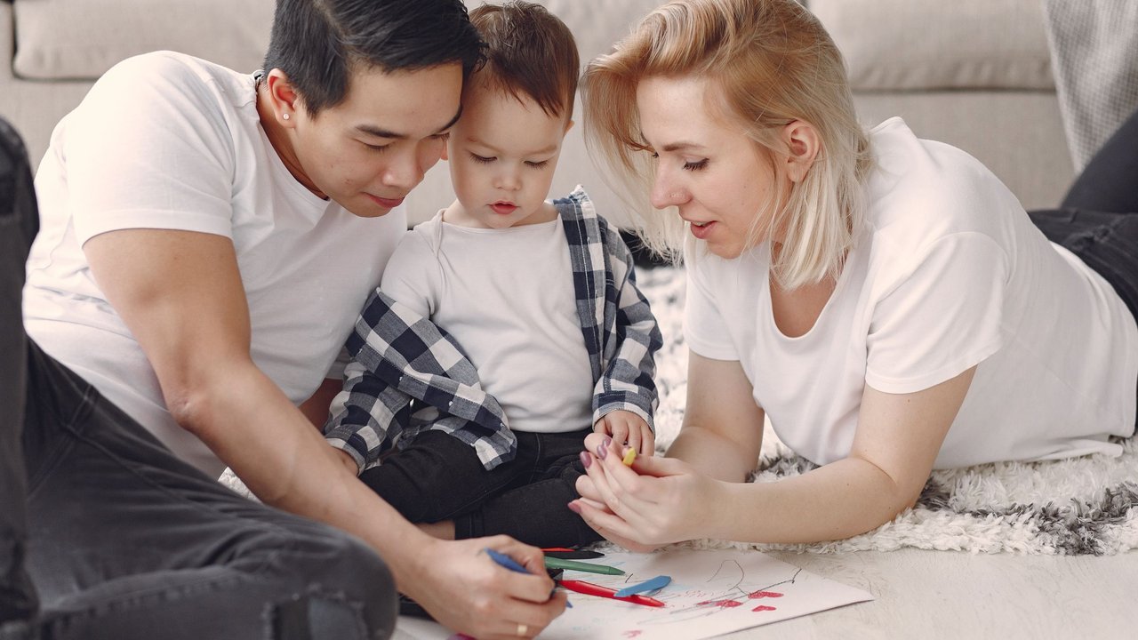 Pai, mãe e filho pequeno desenham juntos no chão da sala de casa
