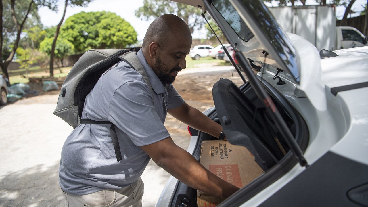 Servidor da Justiça Eleitoral retira caixa de urna eletrônica do porta-malas de um carro